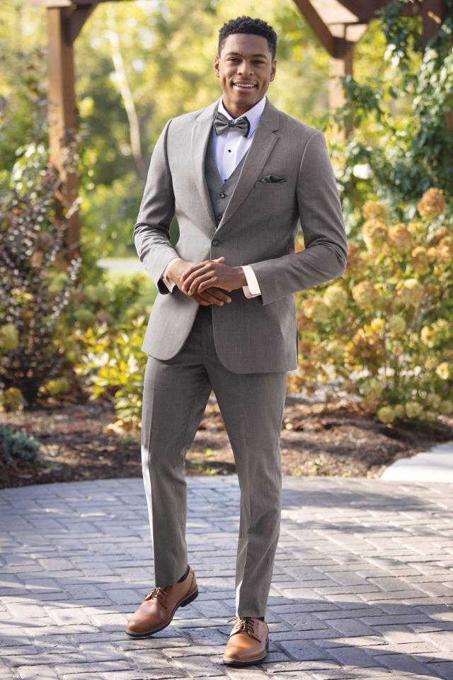 Man wearing Michael Kors Medium Grey suit and matching vest and bow tie standing outside in front of a trellis